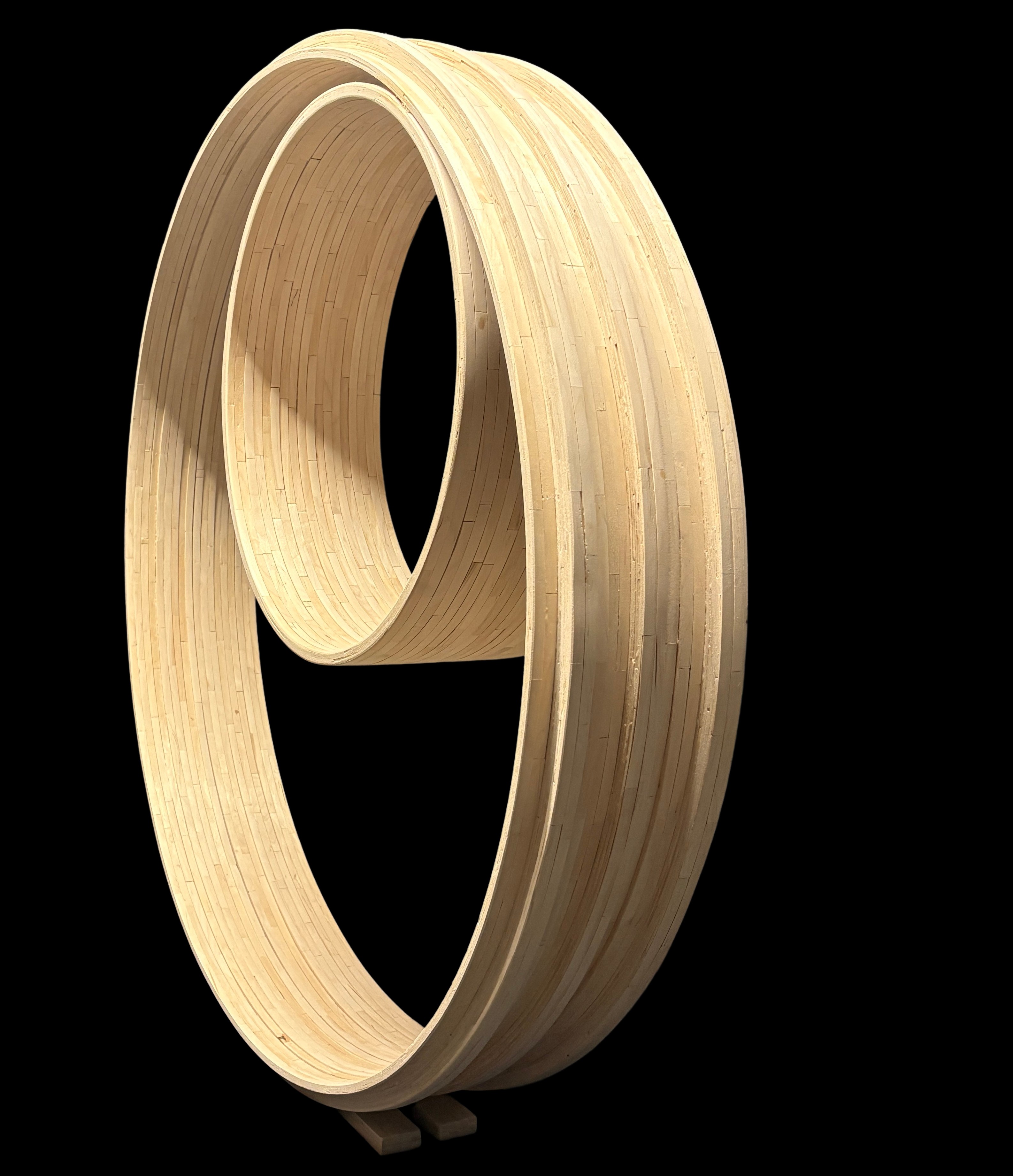 Becoming — two craft stick loops, one large and one small, nested off-center in a single sculpture standing on two small blocks