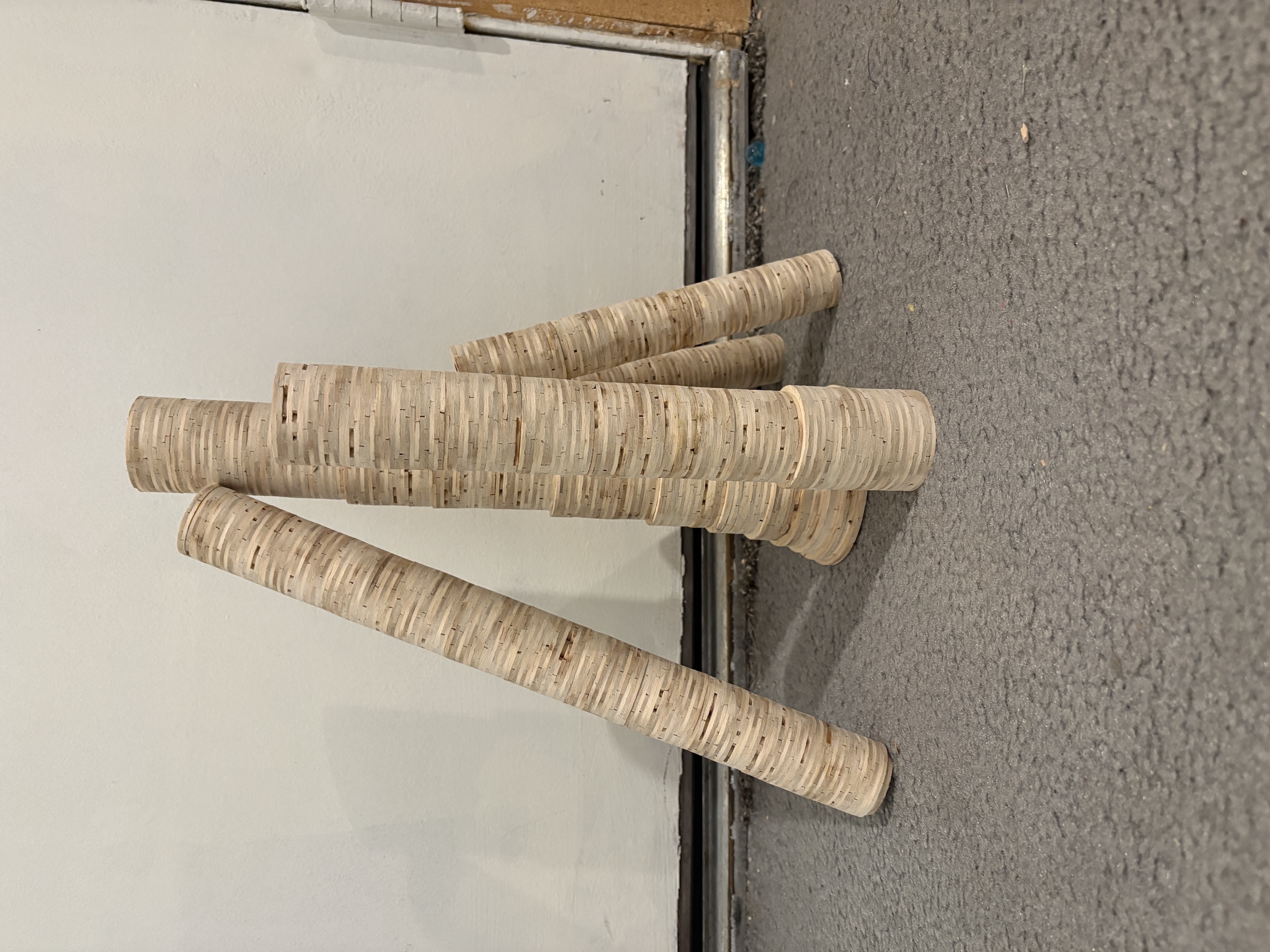 Two columns of stick rings on a wood floor, one stained amber and one pale, laid out along yellow tape guides